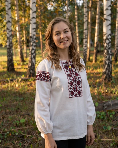 Belarusian woman wearing a traditional embroidered blouse standing in a birch forest, showcasing the natural beauty and rich cultural heritage of Belarusian women